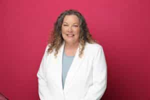 Kris Cesena is wearing a white jacket in front of a fuchsia background.